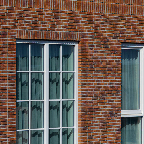 Houten kozijnen voor 47 woningen en 28 appartementen in Gouda, in de wijk Het Carré van Westergouwe. Foto van de de ramen van een woning.